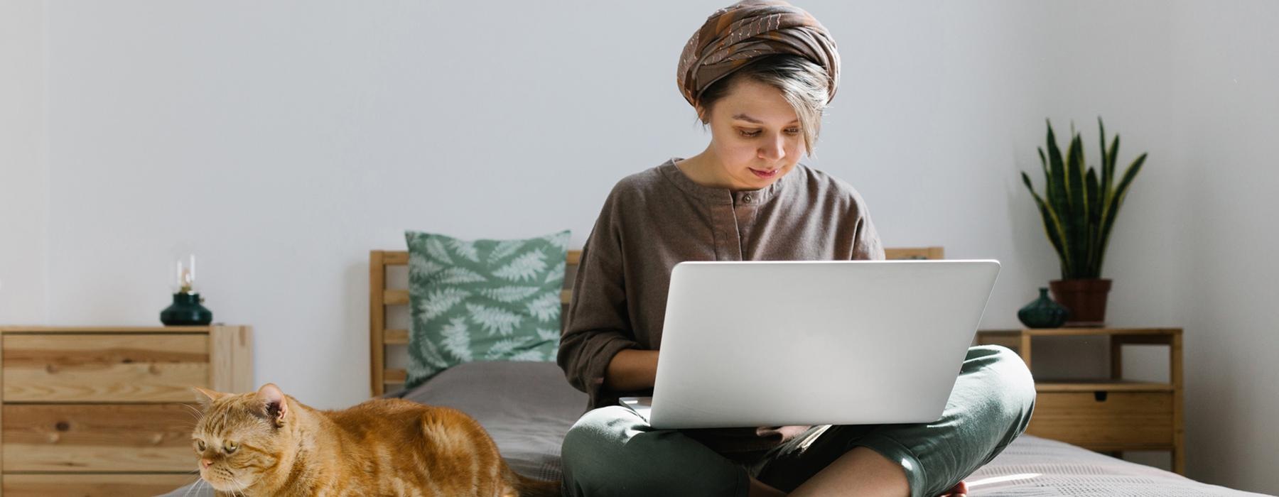 a child sitting on a bed with a laptop and a cat