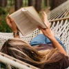 a person lying in a hammock reading a book